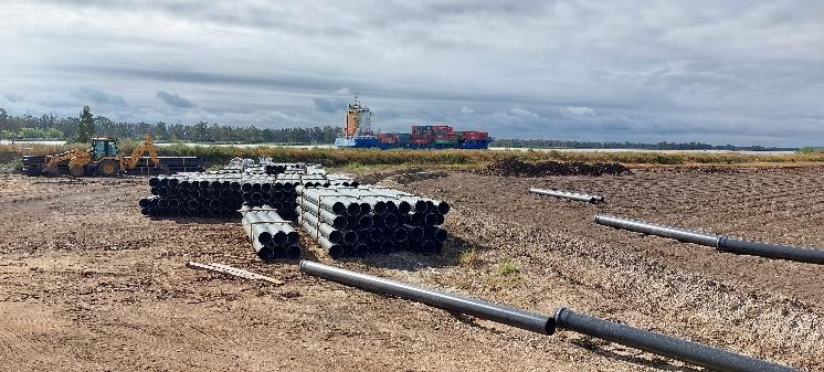 Campo de tierra con grandes pilas de tuberías negras en primer plano.