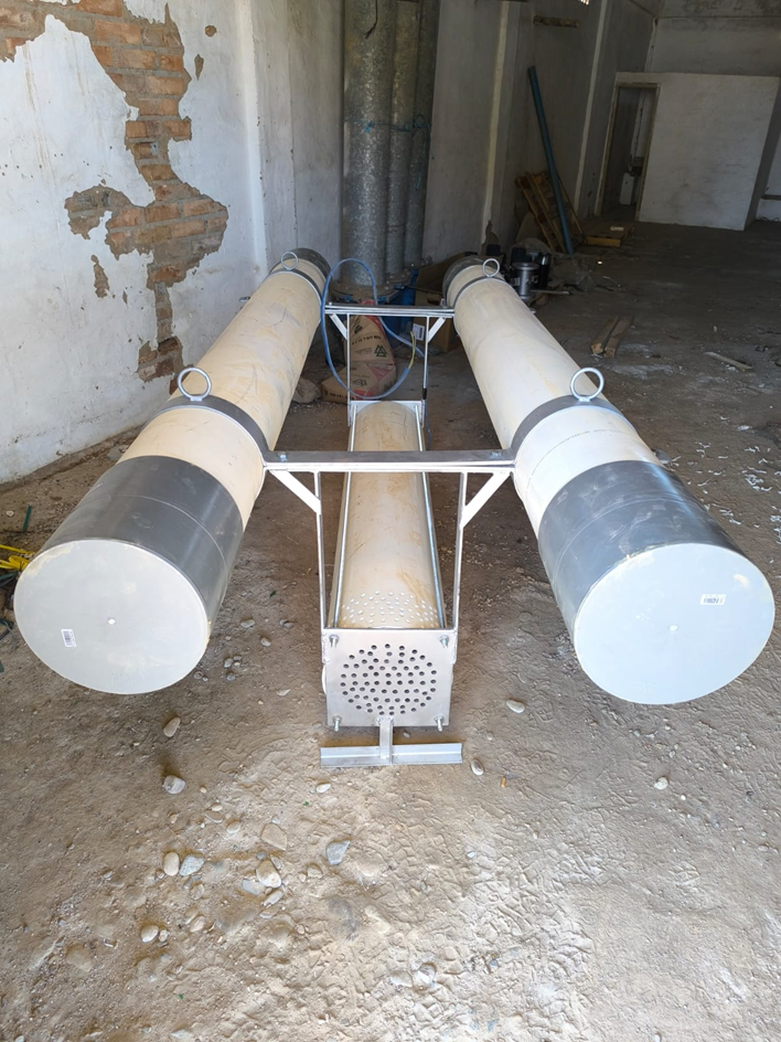 Equipo con dos grandes flotadores cilíndricos beige y grises, y una estructura central metálica con rejilla perforada, probablemente para bombeo o dragado.