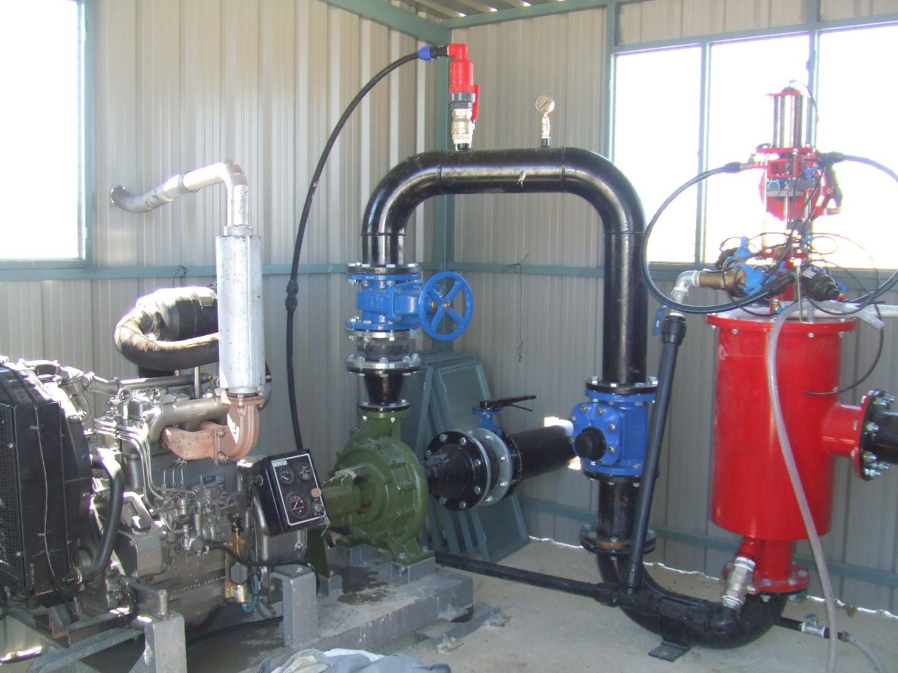 Sala de bombeo industrial con motor diésel, bomba de agua verde, tuberías negras y rojas, y válvulas azules.