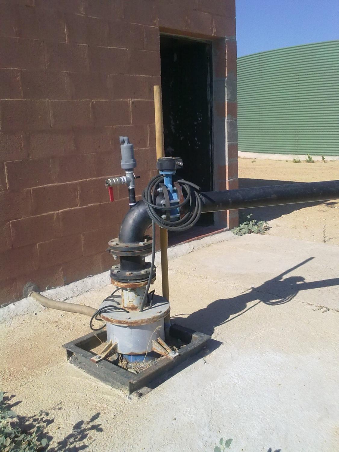 Sistema de bombeo de agua con tuberías negras y sensor, instalado en el exterior junto a una pared de ladrillo.