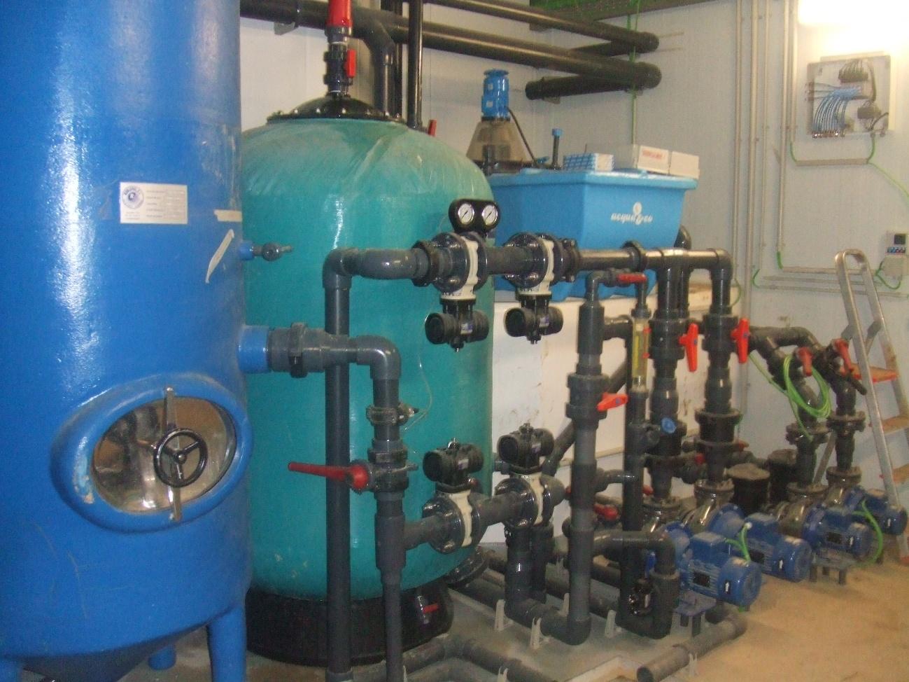 Sistema de filtración de agua con grandes tanques, múltiples tuberías, válvulas, y bombas en una sala de tratamiento.