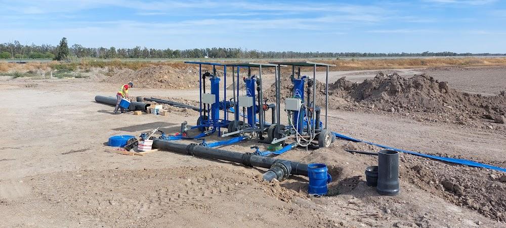 Sistema de filtración o bombeo de agua móvil con múltiples unidades azules sobre ruedas, instalado en un terreno en construcción o campo agrícola.
